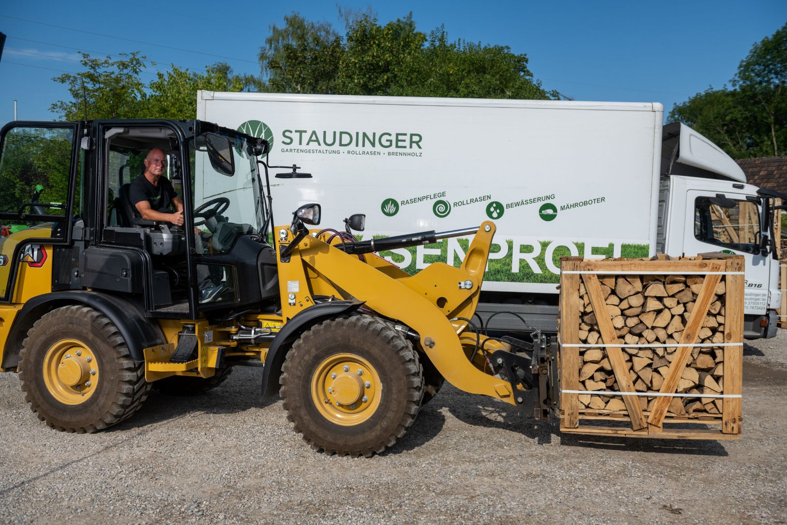 Radlader mit einer Kiste Brennholz vor dem Staudinger-Lkw