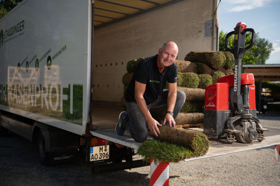 Klaus Staudinger kniet mit einer Rolle Rollrasen an der Ladefläche des Lkw